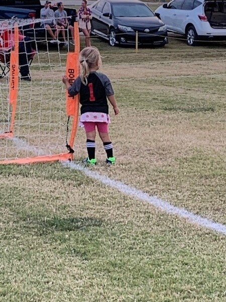 Youth soccer player with her arm around a goal post.