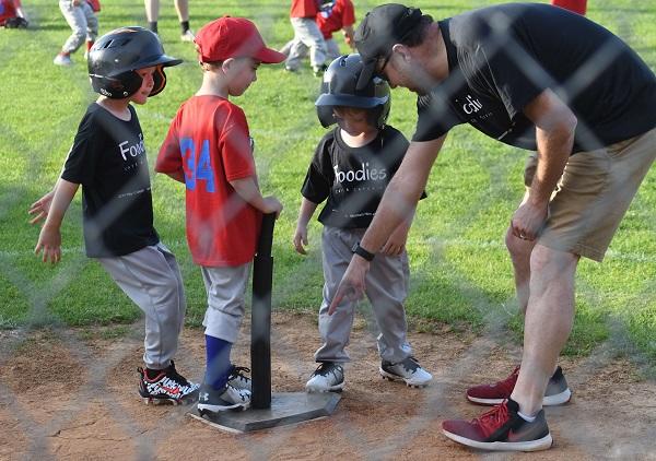 Coach showing young boys how to bat using a tee in baseball