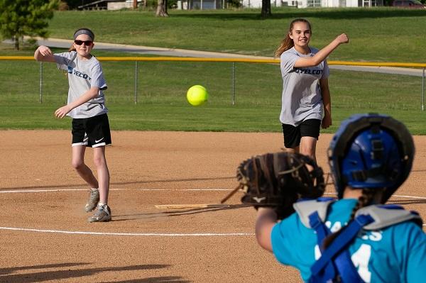 Two girls practicing with the catcher on the softball field
