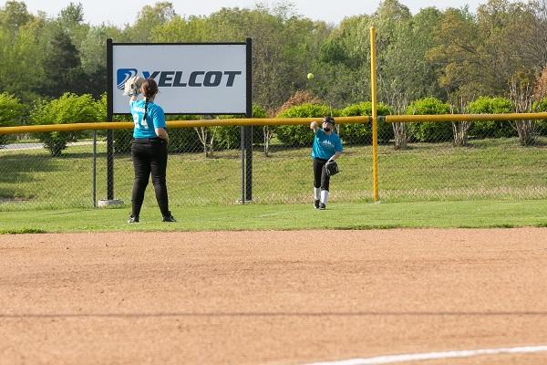 Two girls in the outfield tossing the ball back and forth
