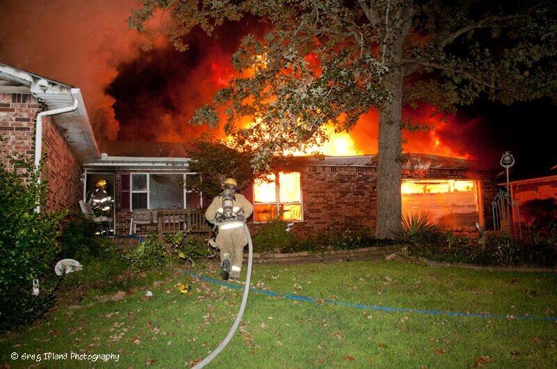 Fireman with hose in front of fully engulfed house